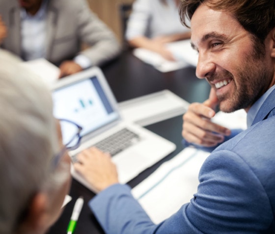 A man wearing a suit sitting in front of a laptop computer discusses Rimini Street solutions for business services and professional services.